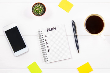 Notepad with the text: the plan. White table with telephone, cactus, paper for notes, coffee mug.