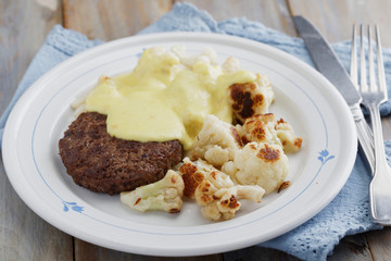 Meat burger with cauliflowers under cheese sauce