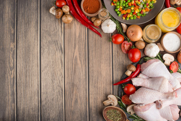 Vegetables with raw chicken legs on a wooden texture. Top view, with an empty space under the inscription or advertisement.