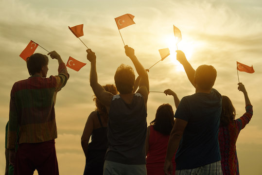 Happy Turkish Family With Flags. Patriotic People Raising Flags To The Evening Sky, Back View.