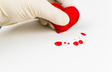 The concept of a broken heart. A hand in a rubber glove compresses the heart and blood stains around.