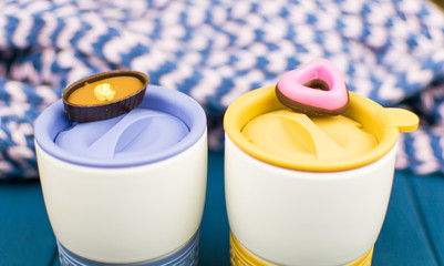 Romantic coffee break. Two thermocovers with sweets on lying caps.