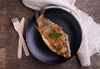 fried fish (carp) on a black plate decorated with parsley