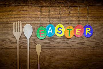 Easter. wooden brown background. The inscription hangs on the twine in the form of eggs. the letters are colored with colored pencils. wooden fork and spoon.