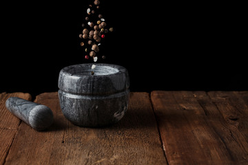 Marble mortar on old wooden table on black background with copy space. Pepper seeds fall into the mortar. freezer food