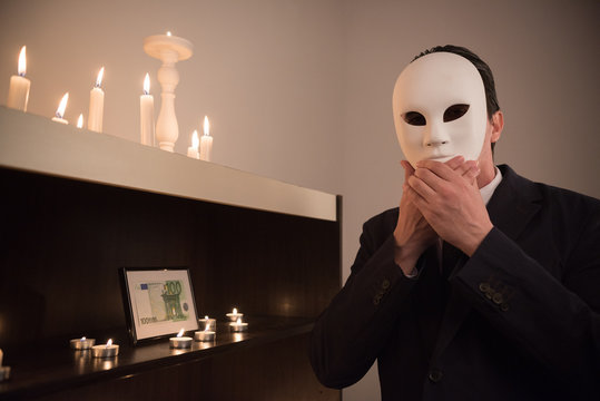 man in suit with mask on his face next to altar with money in frame 