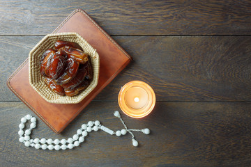 Table top view aerial image of decoration Ramadan Kareem holiday background.Flat lay date in wood basket with white rosary & lighting.The holy book of Koran on modern rustic brown wood at office desk.