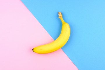 Single yellow banana over a pink and blue background. Top view, minimal concept. © Jenifoto