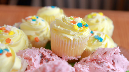 Miniature cupcakes with yellow frosting in front of pink black cherry ice cream on a wood table