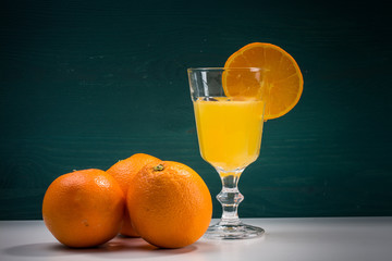 Orangescheibe am Glas mit Orangensaft und Orangen links
