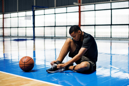 African American teenage boy tying his shoe laces on a basketball court