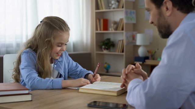 Smart daughter writing in exercise book, caring daddy stroking kids hair