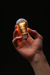 Glowing light bulb in hand on a dark background. © o_shi
