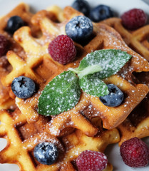 Belgian waffles with blueberries, raspberries and powdered sugar on wooden table.