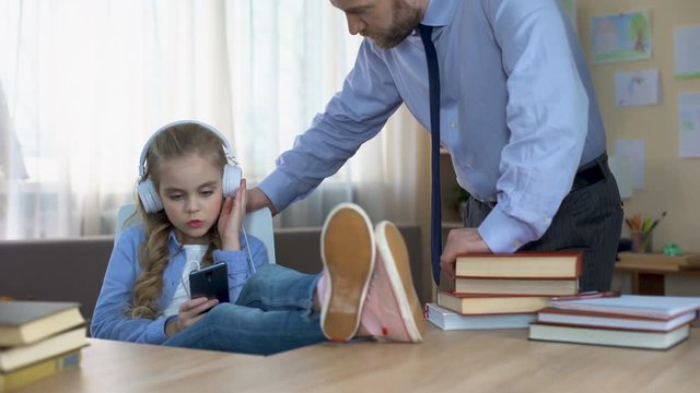 Disobedient girl in headphones listening to music on smartphone, ignoring dad