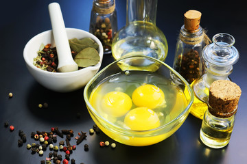 chicken eggs in a glass bowl, spices, bottled oil on a dark background.