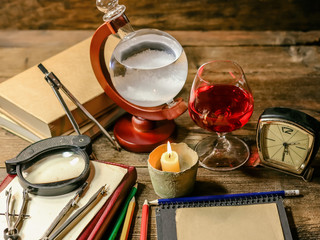pencils, notebook, books, compasses, a glass of wine and an ancient barometer on a wooden table....