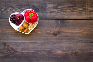 Obraz na płótnie Canvas Food which help heart stay healthy. Vegetables, fruits, nuts in heart shaped bowl on dark wooden background top view copy space