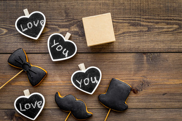 Fototapeta premium Gift for man on birthday. Gift box among cookies in shape of moustache, hat, bow tie and hearts with lettering love you on dark wooden background top view copy space
