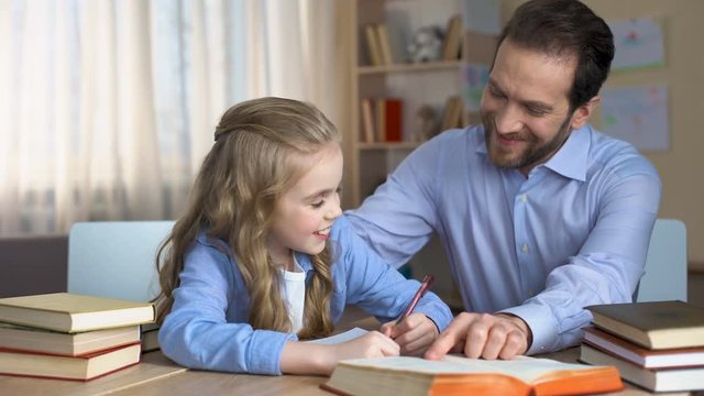 Happy female child doing homework with her caring daddy, support and love