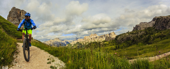 Tourist cycling in Cortina d'Ampezzo, stunning Cinque Torri and Tofana in background. Man riding MTB enduro flow trail. South Tyrol province of Italy, Dolomites.