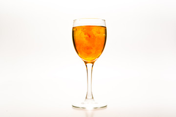 Orange food coloring diffuse in water inside wine glass with empty copy-space area for slogan or advertising text message, over isolated white background.