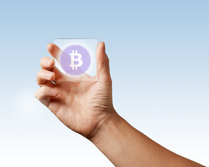 A man's hand holds a transparent digital screen with a bitcoin icon ns blue background