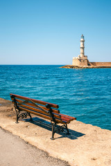empty bench in the harbor with lighthouse in the background, Crete, Chania