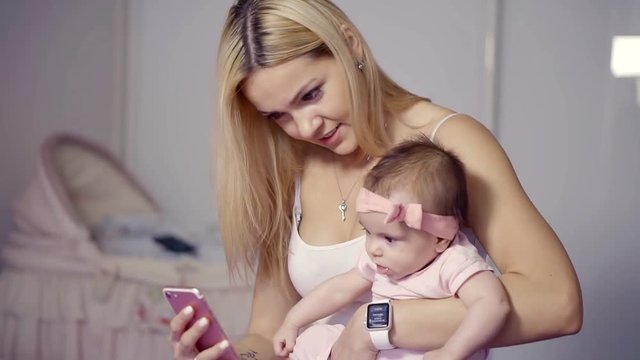 a young mother holding her daughter, who plays with a smartwatch and takes photos on a mobile phone