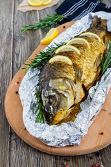 Large baked carp with herbs, lemon and spices in foil on a wooden background. Top view