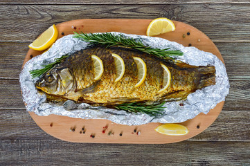 Large baked carp with herbs, lemon and spices in foil on a wooden background. Top view