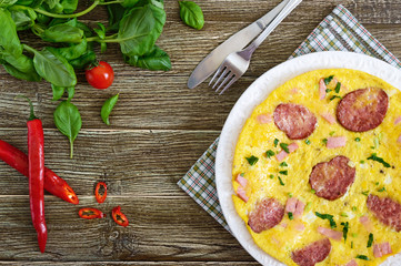 Omelette with ham, salami, cheese and greens on a plate on a wooden background. Breakfast. Top view.