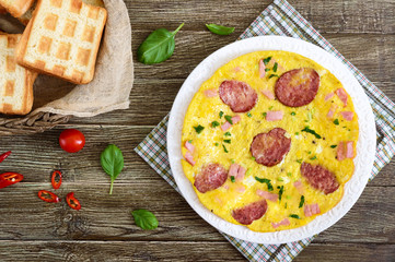 Omelette with ham, salami, cheese and greens on a plate on a wooden background. Breakfast. Top view.