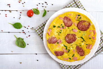 Omelette with ham, salami, cheese and greens on a plate on a white wooden background. Breakfast. Top view.