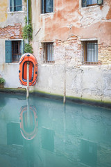 orange inflating rubber boat hanging on a wooden pole  above a green turquoise canal in venice, Italy