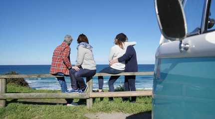 Senior friends on a road trip looking at the ocean, sit on fence © goodluz