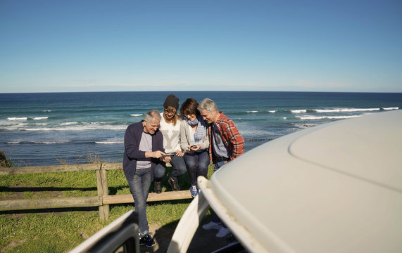 Group of senior people using smartphone by the sea, road trip