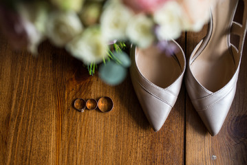 Golden wedding rings, engagement rings and a bridal beige shoes on brown background. Bridal accessories.