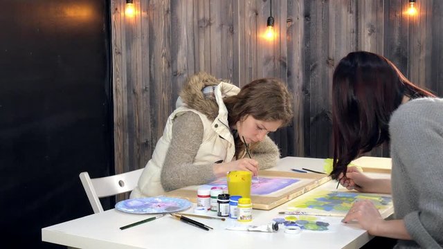 Two adult women paint with colored acrylic paints in an art school