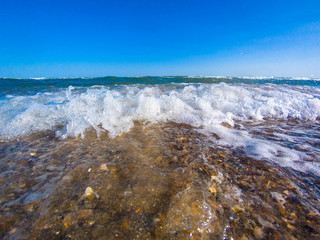 Foam on a crest of a sea wave against a blue sky. Sea waves roll on to shore. Sea foam. Stormy sea. Closeup