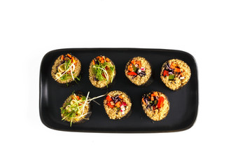 Vegan sushi rolls with quinoa and vegetables  on a black plate, white background, isolate. Vegan Healthy Food Concept.
