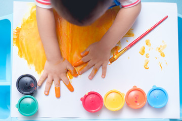 Bird eye view / Top view of little Asian 18 months / 1 year old toddler baby boy child finger painting with hands and watercolors, kid painting at home, Creative play for kids and toddlers concept