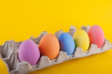 Five wooden colored eggs laying in paper container on yellow background