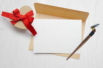 Mockup calligraphic feather an envelope with letter and a gift with a red bow, greeting card for Valentines Day with place for your text. Flat lay, top view photo mock up