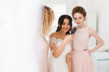 bride and bridesmaid discussing photos on smartphone. Morning preparation