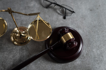Law and Justice concept. Mallet of the judge, glasses, scales of justice. Gray stone background, reflections on the floor, place for typography. Courtroom theme.