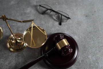 Law and Justice concept. Mallet of the judge, glasses, scales of justice. Gray stone background, reflections on the floor, place for typography. Courtroom theme.