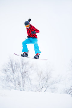 Image of sportive male snowboarder jumping on snowy hill