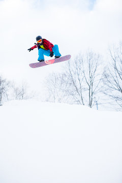 Image of sporty man in helmet with snowboard jumping in snowy resort