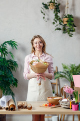 Photo of smiling florist in apron with bouquet of flowers with kraft paper